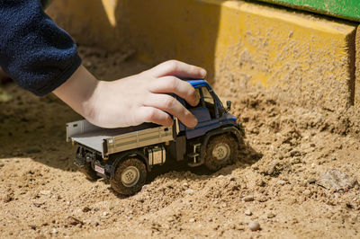 Cropped hand of child playing with toy truck in sand