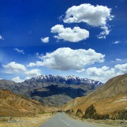 Country road leading towards mountains against cloudy sky