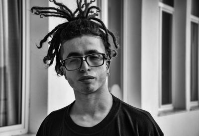 Close-up portrait of young man with dreadlocks standing by windows