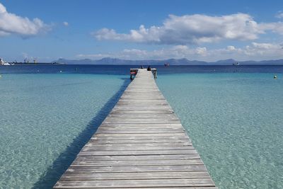 Empty jetty leading to sea against cloudy sky