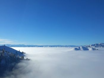 Scenic view of a sea of,clouds with snowy mountains protruding against clear blue sky