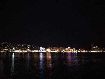 Illuminated buildings by river against sky at night