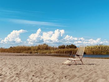 Deck chairs on sand at beach against sky