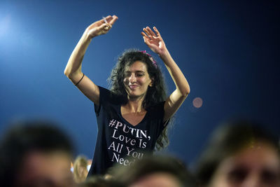 Portrait of young woman with arms raised against blue sky