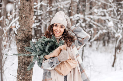 A cute girl with her hand on her hat in a snowy forest holds a package with fir nobilis
