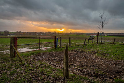 Wooden fence on field against sky during sunset