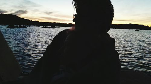 Silhouette man by lake against sky during sunset