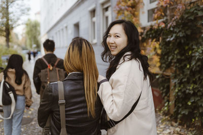 Happy woman looking away while walking with female friend on sidewalk