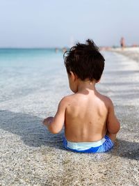Rear view of shirtless boy at beach