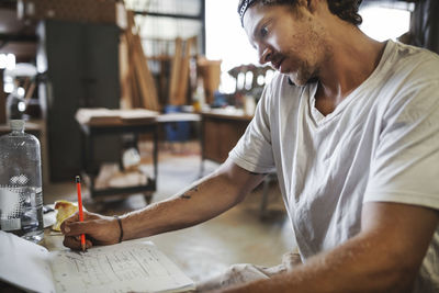 Carpenter using mobile phone while reading document in workshop