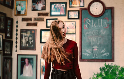 Portrait of woman standing against picture frames at home