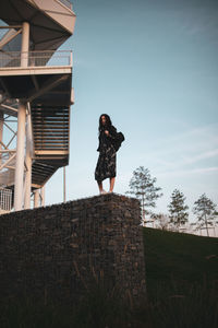 Low angle view of woman standing on stone wall against sky