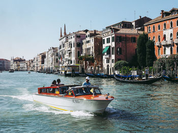 People on boat in city by sea against clear sky