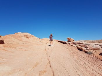 Low angle view of woman standing on rock formation against clear blue sky