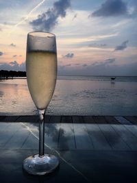 Close-up of beer on table against sea during sunset