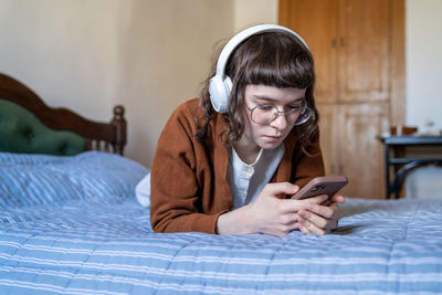 Young woman using mobile phone while sitting on bed at home