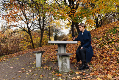 A woman uses a smartphone sitting at a table in an autumn park