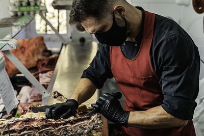 Professional butcher with mask preparing and cutting meat