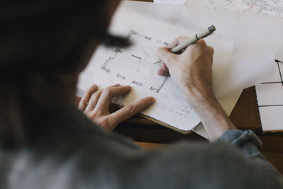 Over shoulder view of male architect sketching blueprint on paper at desk in home office