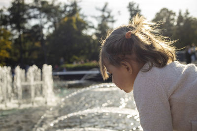 Adorable toddler girl looks fountains in park. weekend family walk. spending time with children