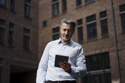 Businessman holding digital tablet while standing against building