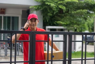 Portrait of delivery man standing at closed gate against buildings