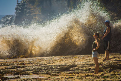 Friends standing on rock formation by splashing waves