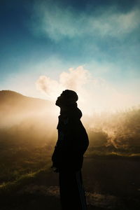 Side view of silhouette man smoking while standing against sky during sunset