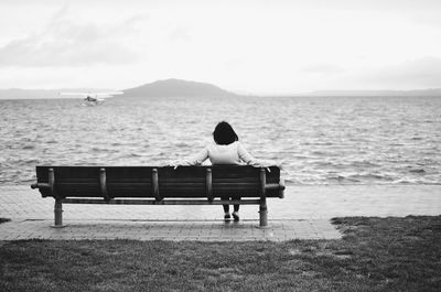 Rear view of woman sitting on beach against sky