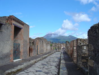 Narrow walkway along buildings and mountains against blue sky