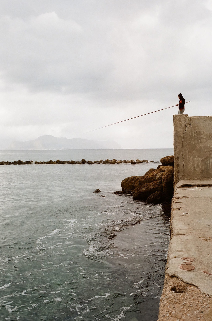 sea, sky, rock - object, cloud - sky, water, one person, men, real people, nature, standing, day, leisure activity, horizon over water, outdoors, scenics, full length, adventure, beauty in nature, one man only, people