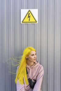 Young woman looking away while standing against metal wall on sunny day