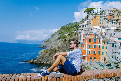 Man sitting by sea against sky