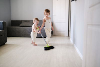 Children siblings with mop sweep floor in bright living room, help with housework 