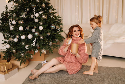 Portrait of young woman sitting on christmas tree