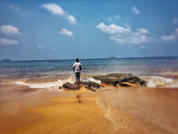 Rear view of man standing on beach against sky