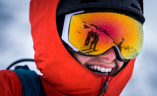 A woman laughing with goggles and a jacket hood on