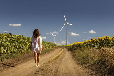 Rear view of woman walking on road towards windmills