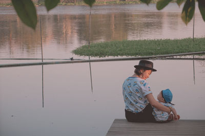 Rear view of mother with baby sitting on pier over lake