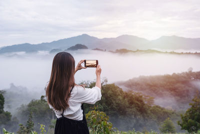 Rear view of person photographing against sky