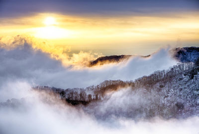 Scenic view of mountains in foggy weather at sunset