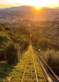 Vertical shot of grass covered pathway over a city in a valley with the sun shining in background