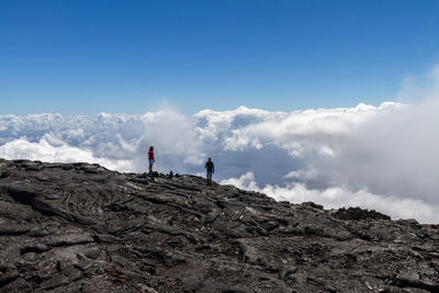 Tourists on mountain against cloudy sky