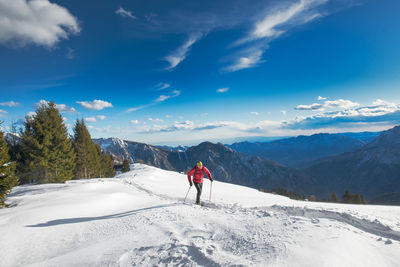 Rear view of man walking on snow covered mountain against sky