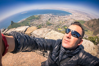 Young man wearing sunglasses standing on mountain against sky