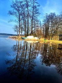 Reflection of bare trees in lake against sky