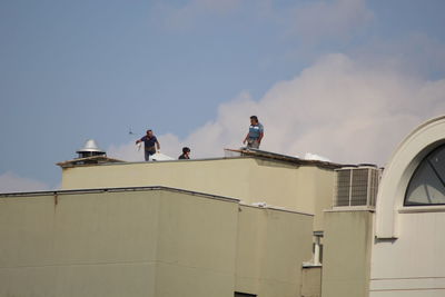 Low angle view of people working on building against sky