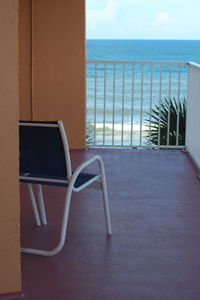 Empty chairs and table by sea against sky