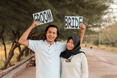 Portrait of smiling young couple holding texts while standing on road