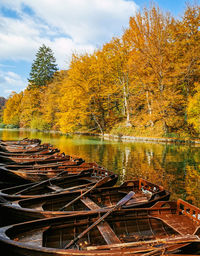 Brown wooden boats moored by pier on idyllic lake surrounded with beautiful forest in autumn